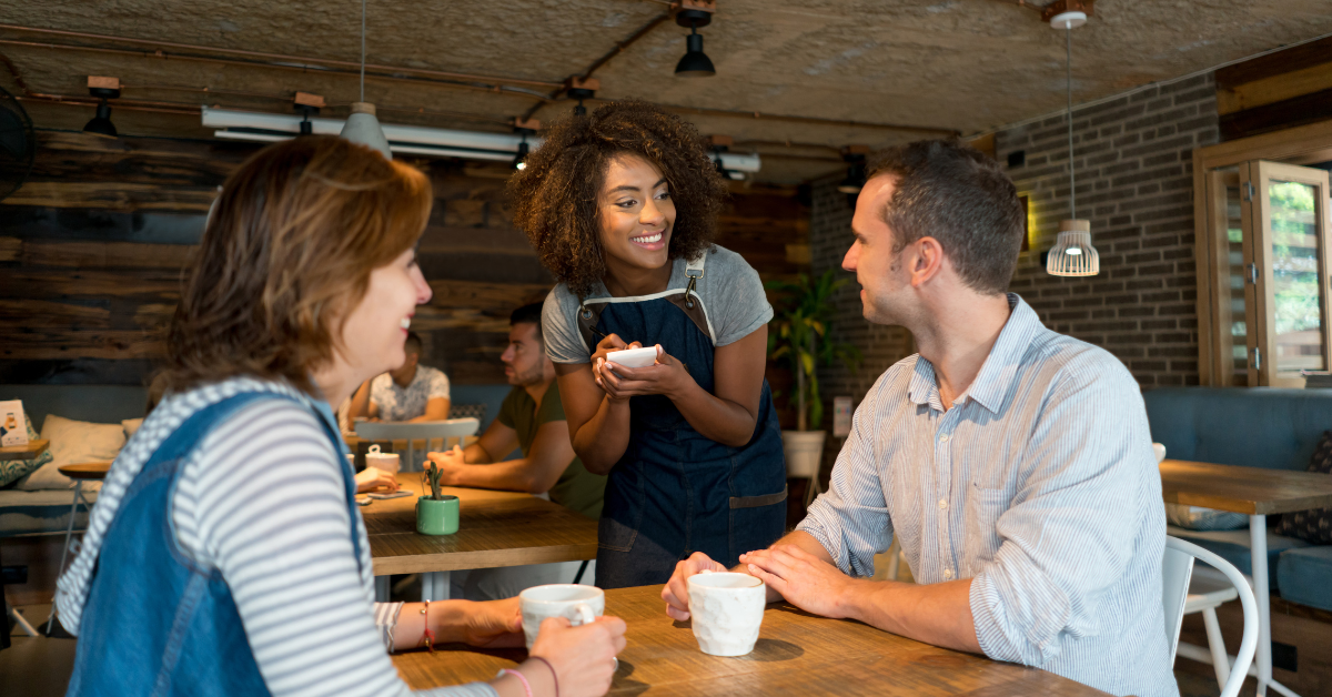 Smiling waitress taking an order from a couple at a café, showcasing warm hospitality and personalized customer service.