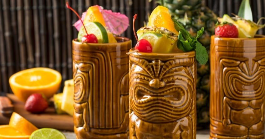 Three ceramic tiki mugs filled with colorful tropical cocktails and garnishes — an example of specialty glassware that adds personality and theme to service.
