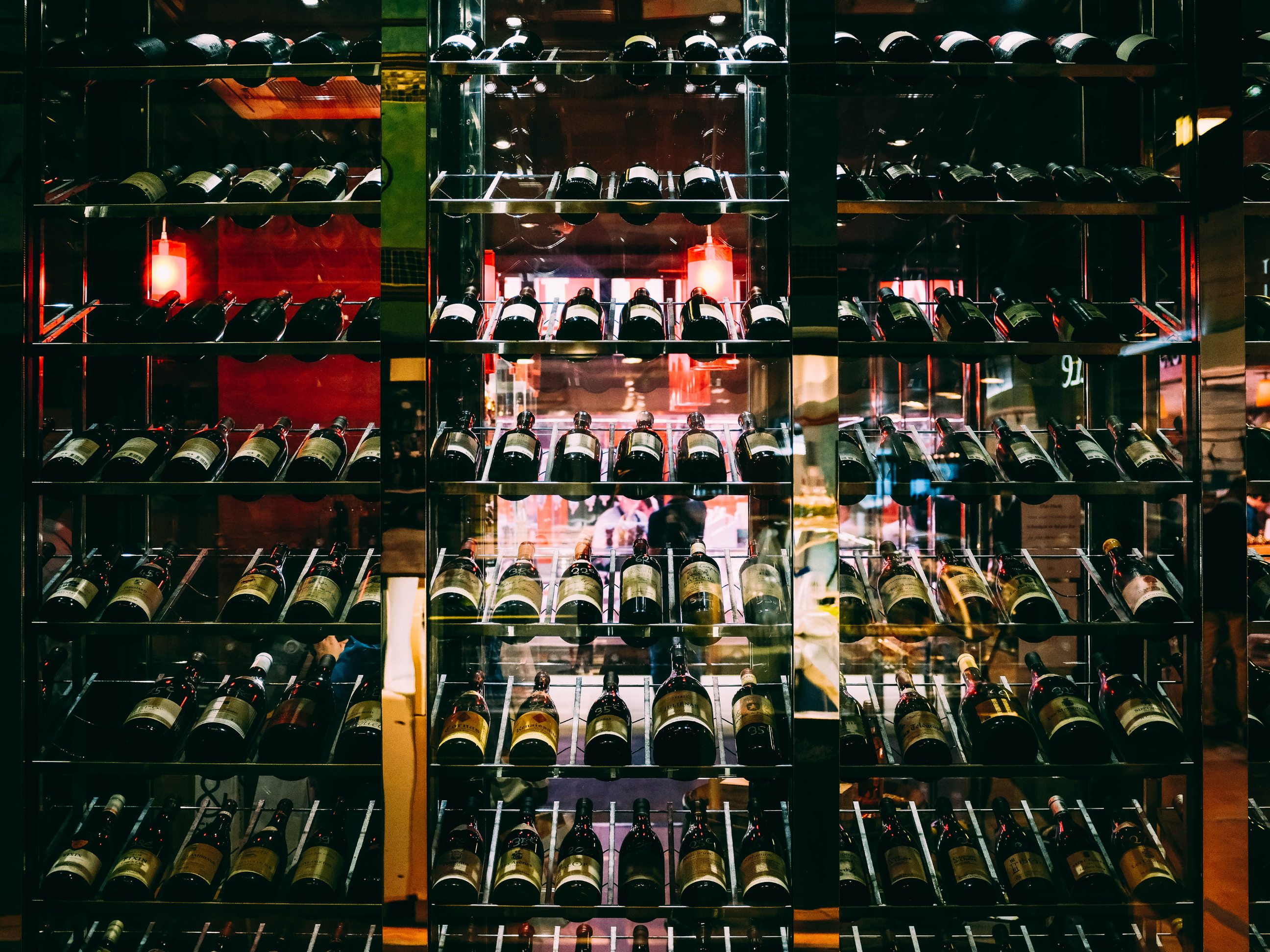 Close-up of a backlit wine storage rack filled with assorted bottles, arranged neatly in rows, showcasing a stylish and organized beverage inventory.