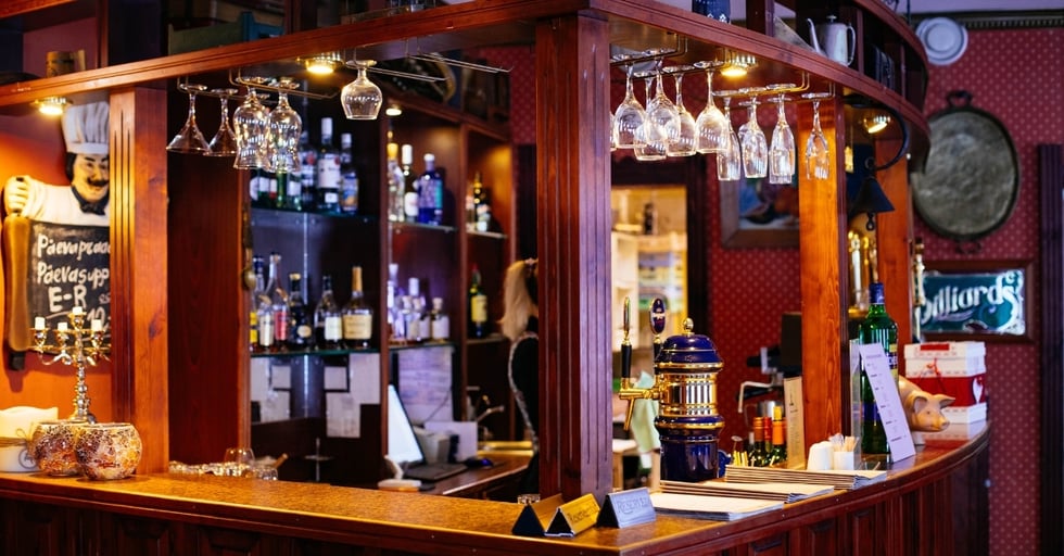 Cozy bar interior with wooden counter, hanging glasses, and liquor bottles on display.