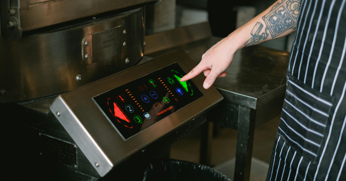 Chef using digital touchscreen controls on modern restaurant kitchen equipment.