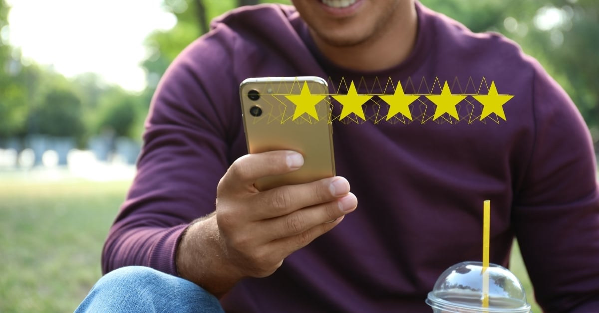 Smiling man leaving a five-star review on his smartphone, representing positive customer feedback and strong online reputation.