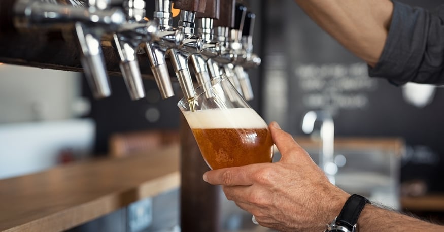 Bartender pouring draft beer from tap system into a glass at a bar.
