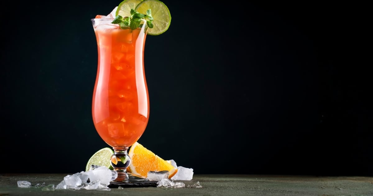 Hurricane glass filled with bright orange cocktail, garnished with lime and mint, emphasizing showmanship and volume control for tropical drinks.