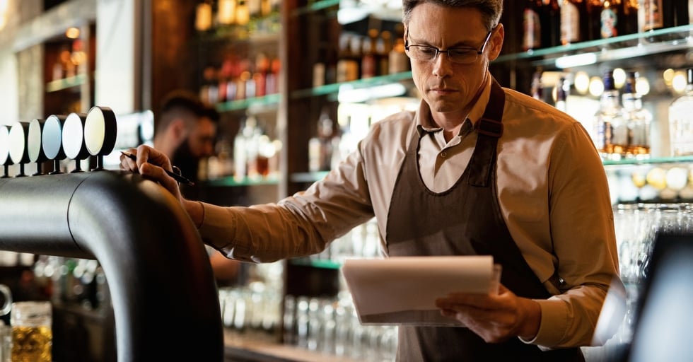 Bar manager reviewing inventory on a tablet, ensuring accurate tracking of safety stock levels to avoid shortages.