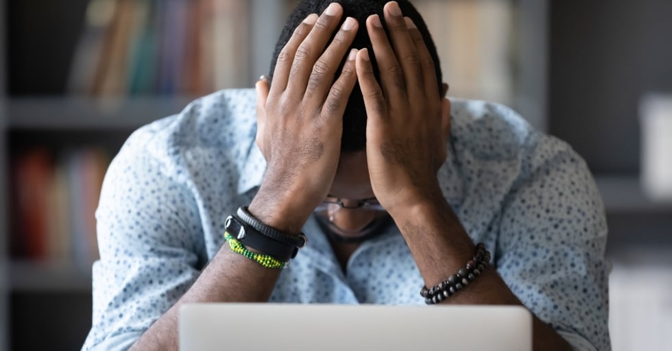 Man sitting at a desk with head in hands, looking frustrated.