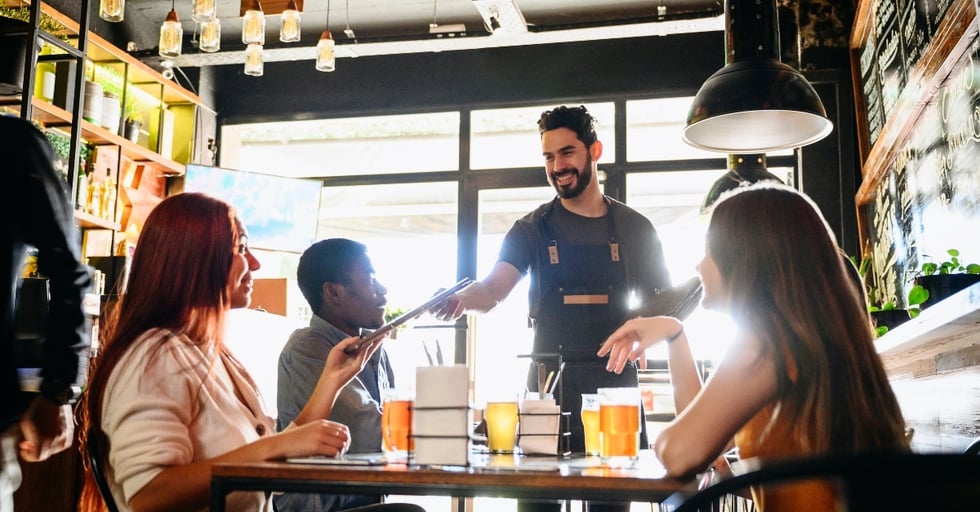 Smiling server taking orders from a group of customers in a restaurant.