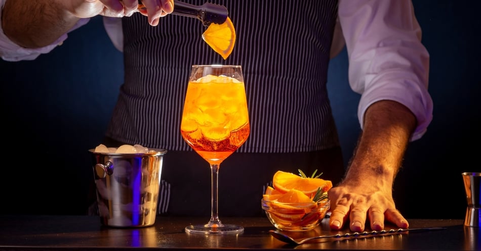 Bartender preparing an orange cocktail with ice and fruit garnish.