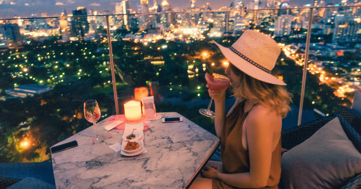 Woman enjoying a cocktail at a rooftop bar with city skyline view at night — highlighting premium restaurant loyalty rewards and exclusive guest experiences.