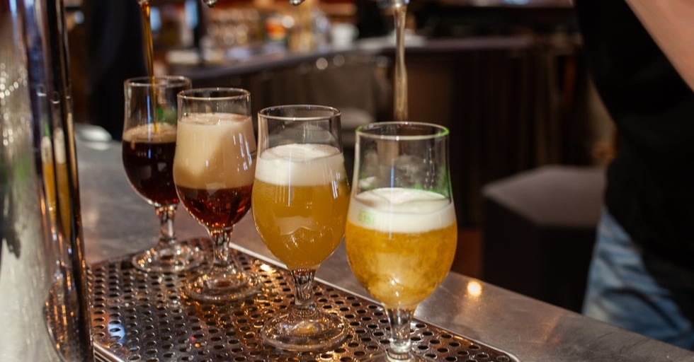Row of draft beers being poured into glasses at a bar counter.