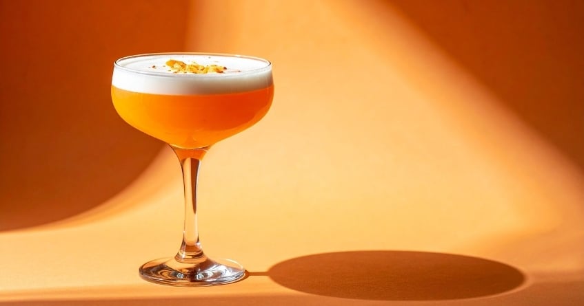 Classic coupe glass with a bright orange cocktail and foam top, demonstrating how bowl shape influences aroma, temperature, and visual appeal.