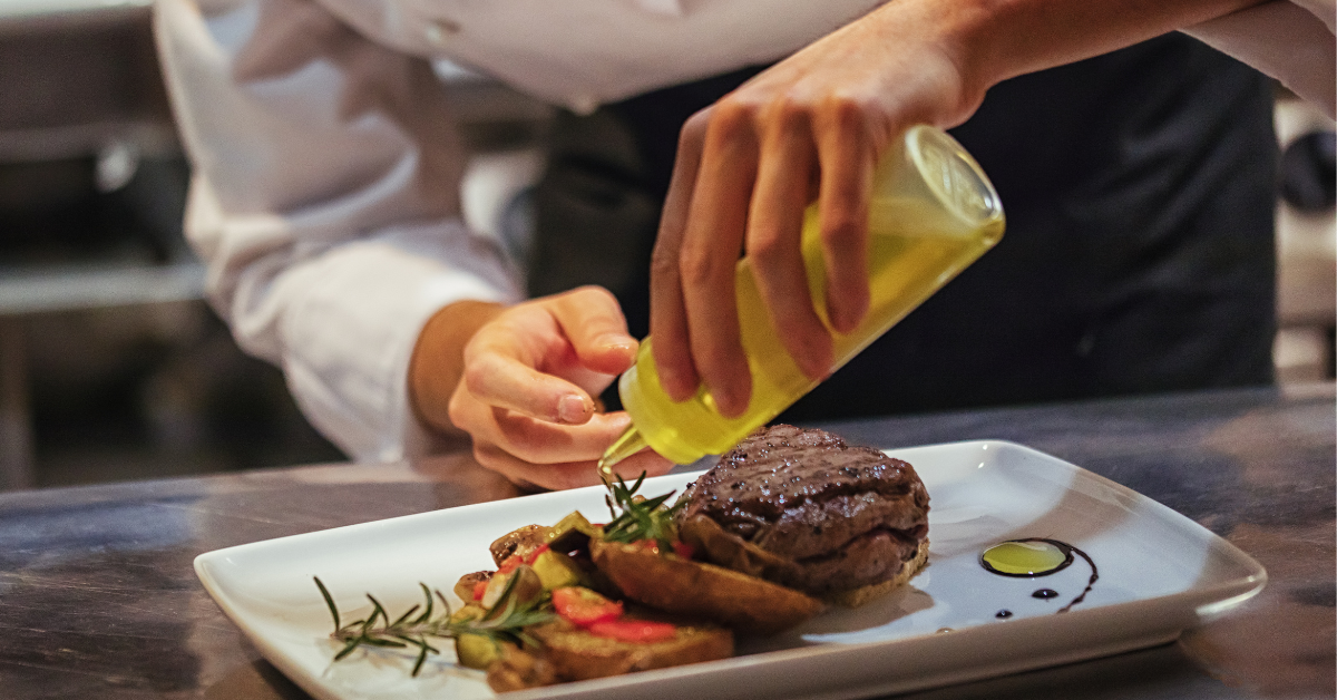 Chef garnishing a steak dish with oil in a fine dining kitchen — a reminder that portion control and plate consistency are essential for accurate food cost management.