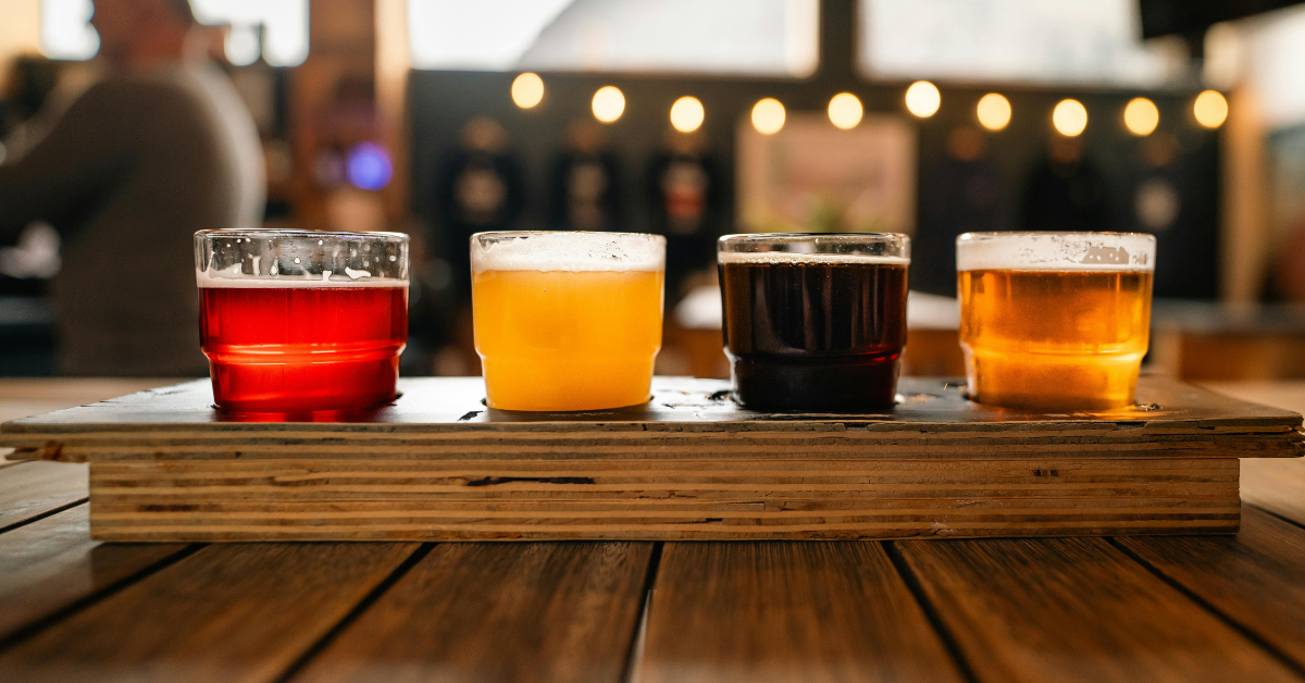 Craft beer flight with four colorful samples on wooden tray in bar setting"