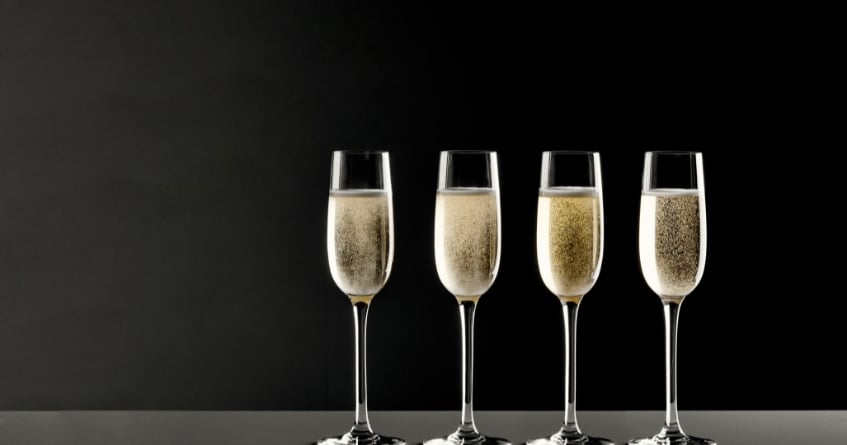 Four Champagne flutes with sparkling wine against a dark background, emphasizing carbonation retention and refined presentation for bubbly cocktails.