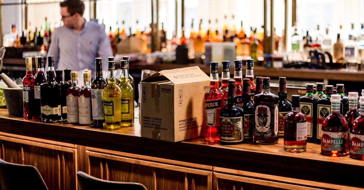 Bar counter stacked with liquor bottles and a delivery box — properly receiving and logging liquor inventory helps reduce shrinkage and improve variance control.