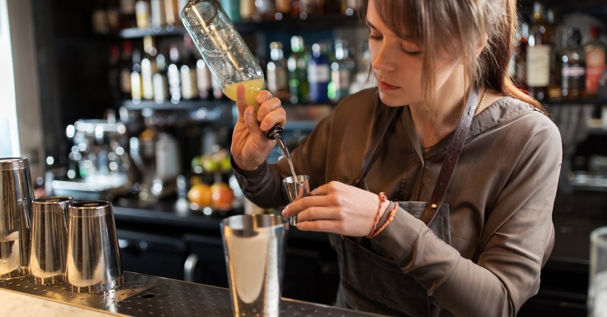 Bartender using a jigger to measure liquor accurately while making a cocktail — demonstrating proper pour control in bar operations.