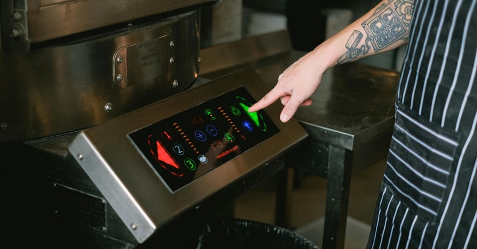 Chef using digital touchscreen controls on modern restaurant kitchen equipment.