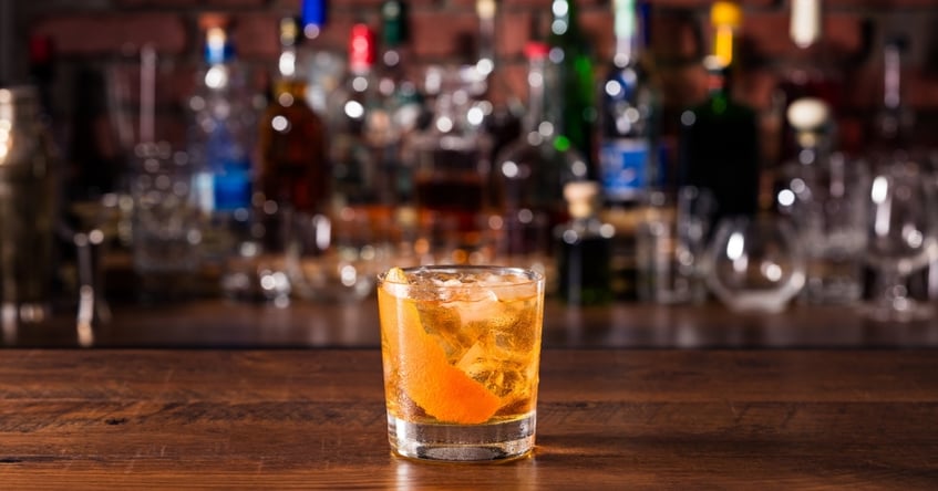 Rocks glass with an Old Fashioned cocktail on a wooden bar, highlighting pour control, ice proportion, and presentation in spirit-forward drinks.