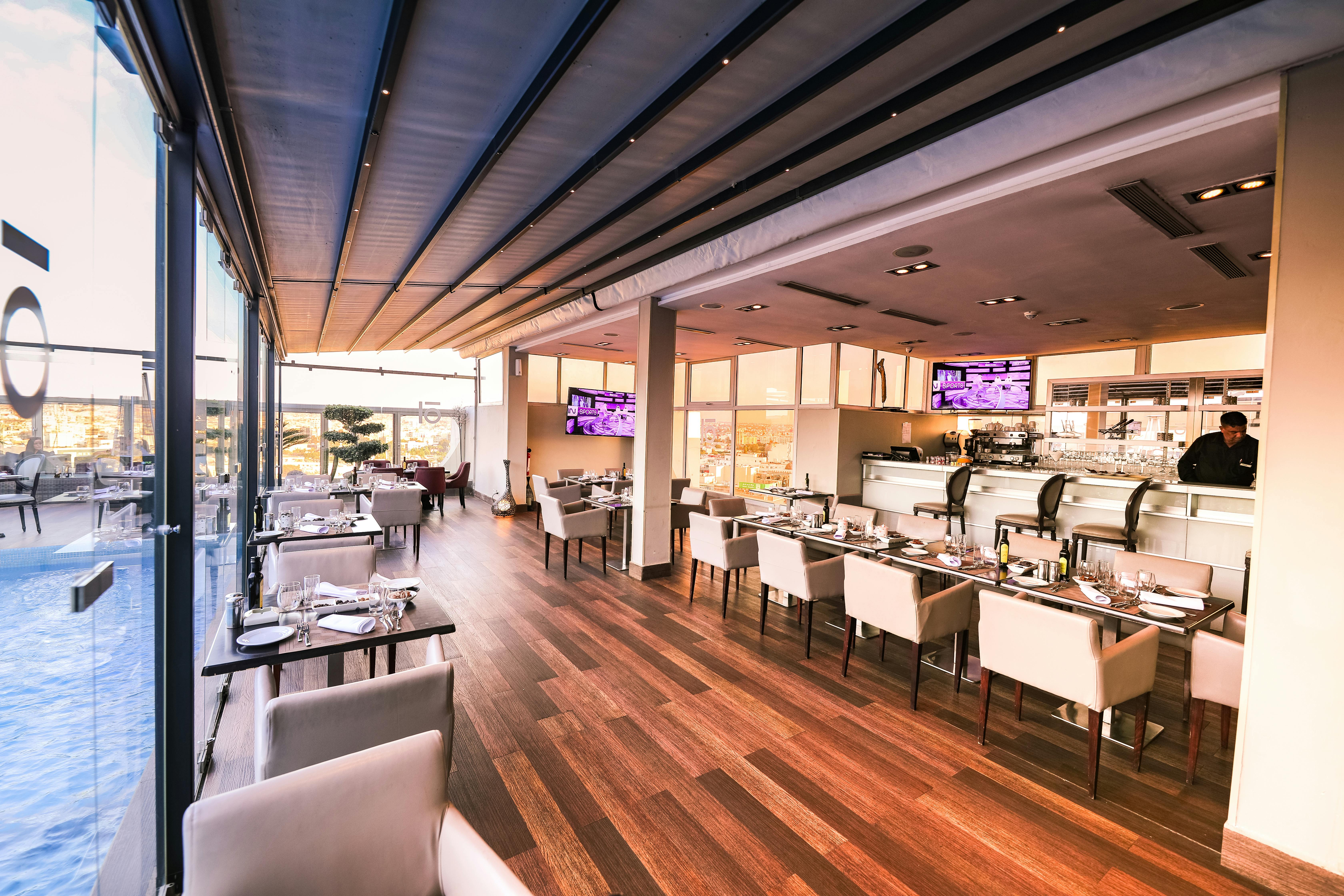 Sleek, modern bar and restaurant interior with wood flooring, white chairs, and flat-screen TVs on the walls.