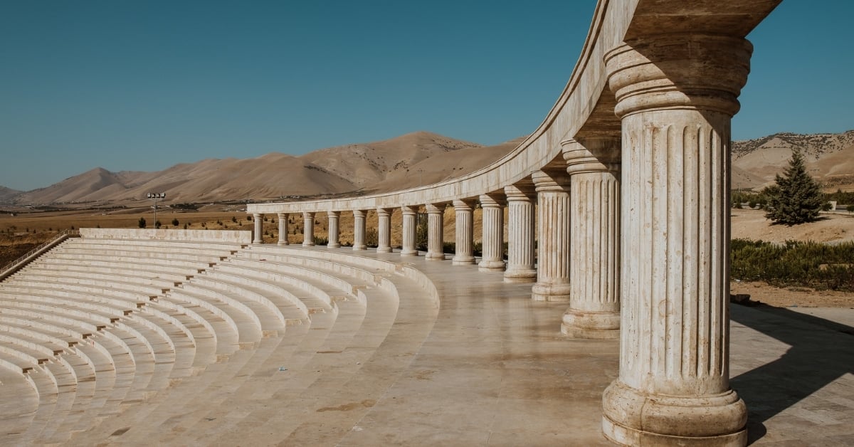 Curved row of stone pillars and amphitheater seating under clear blue sky, symbolizing structure, stability, and lasting foundations.