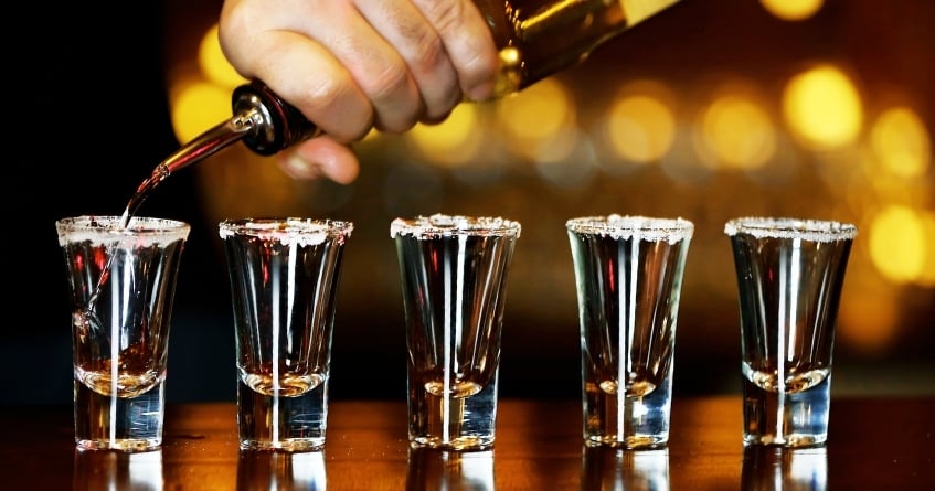 Bartender pouring spirits into a line of rimmed shot glasses, showcasing precision, consistency, and portion control in cocktail preparation.
