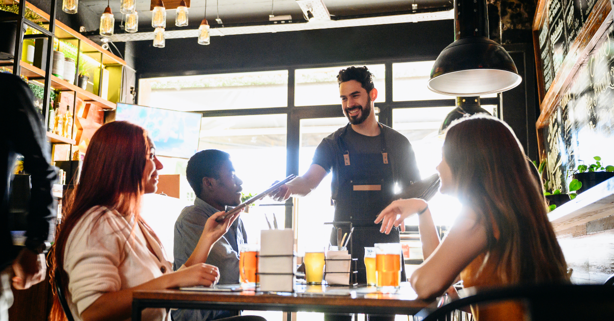 Smiling server handing menus to a diverse group of guests at a casual restaurant, capturing team hospitality and guest engagement.