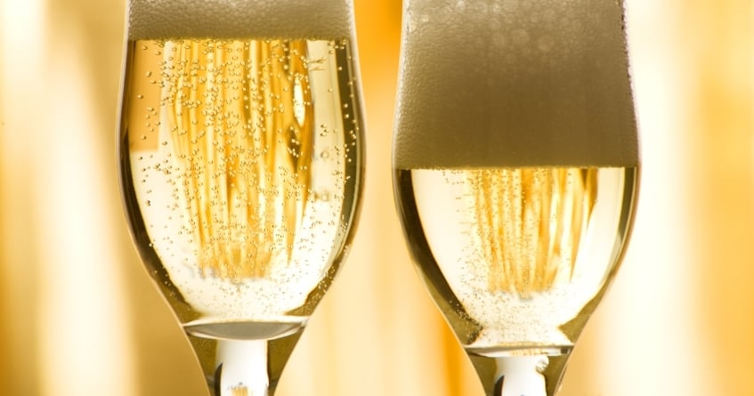 Close-up of two Champagne tulip glasses filled with sparkling wine, showing rising bubbles and foam that highlight the tulip shape’s ability to preserve aroma and carbonation.