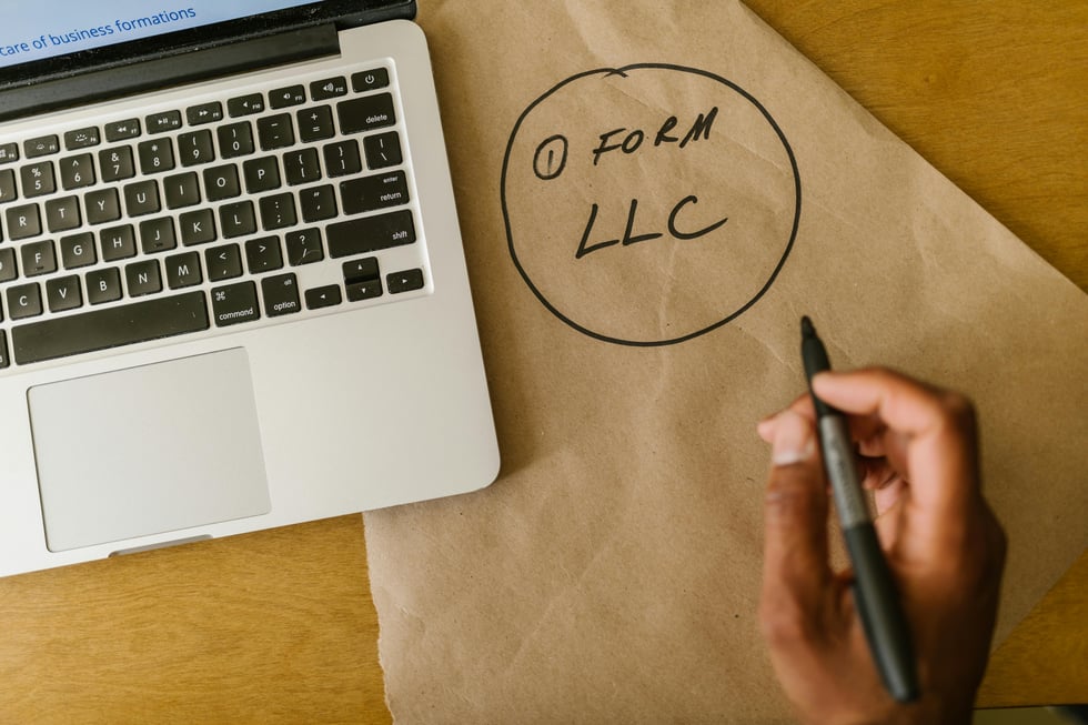 Person writing “Form LLC” on brown paper next to an open laptop—symbolizing small business formation.