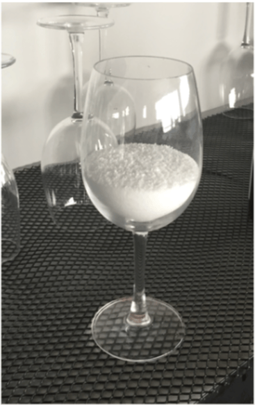 Wine glass filled to standard pour level with dry rice to aid in bartender training for pour accuracy.
