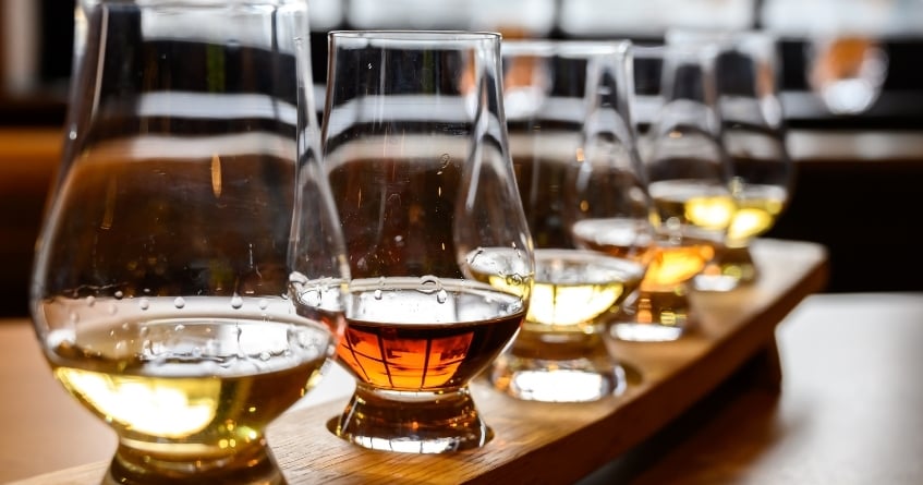 Whiskey tasting flight in Glencairn glasses on a wooden tray, highlighting aroma concentration and portion accuracy in spirit service.