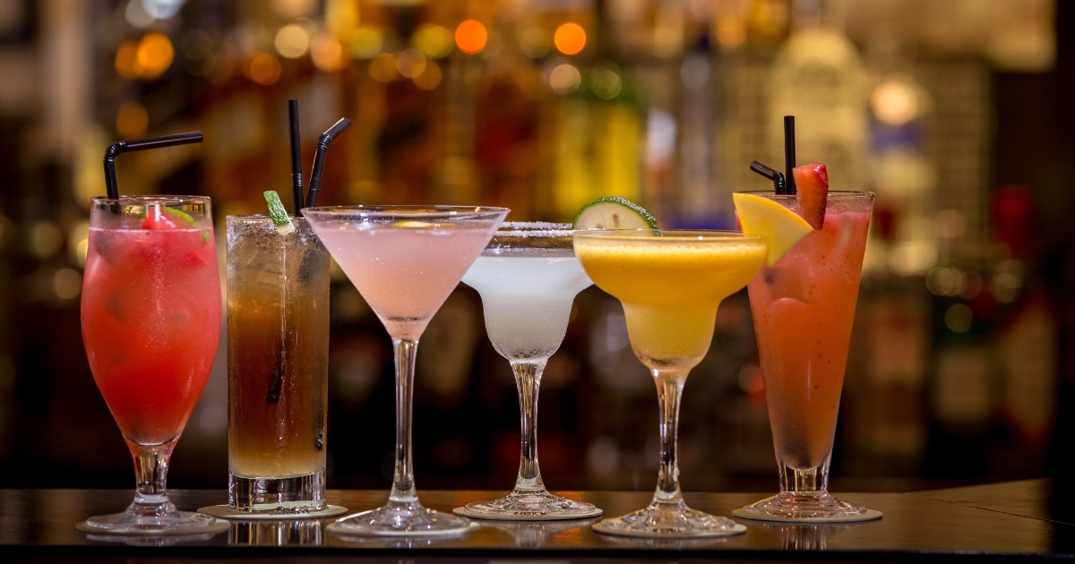 A lineup of colorful cocktails in different glass styles — from martini and margarita to highball and hurricane — illustrating how glass shape and size influence presentation, portion, and guest perception behind the bar.