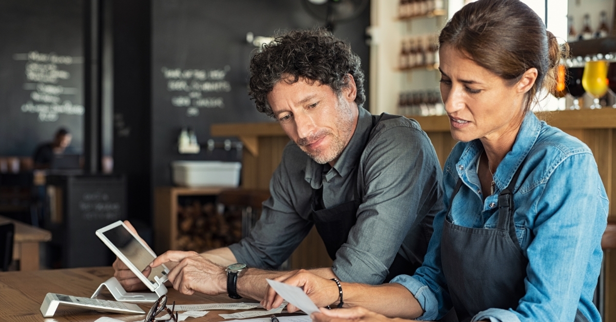 Two restaurant owners reviewing a business plan, using printed documents and a tablet.