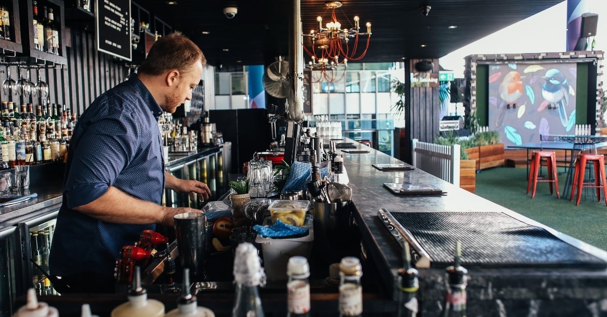 Bartender preparing drinks behind a modern bar, highlighting the importance of safety stock to keep essential supplies on hand during busy service.