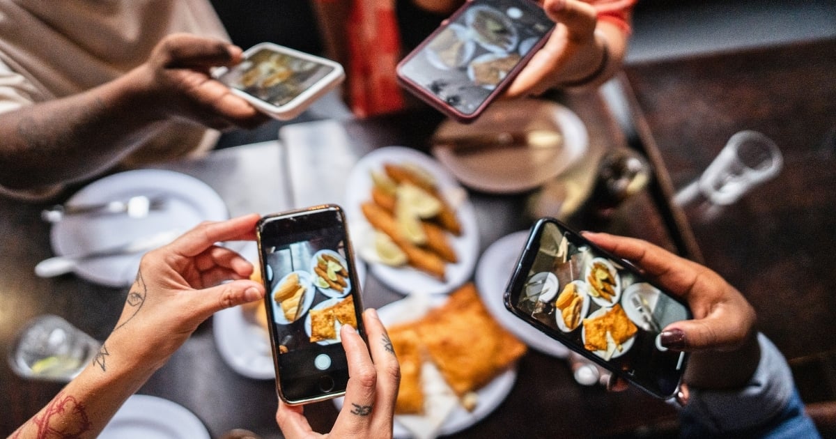 Diners using smartphones to photograph food, representing user-generated content and organic restaurant promotion.