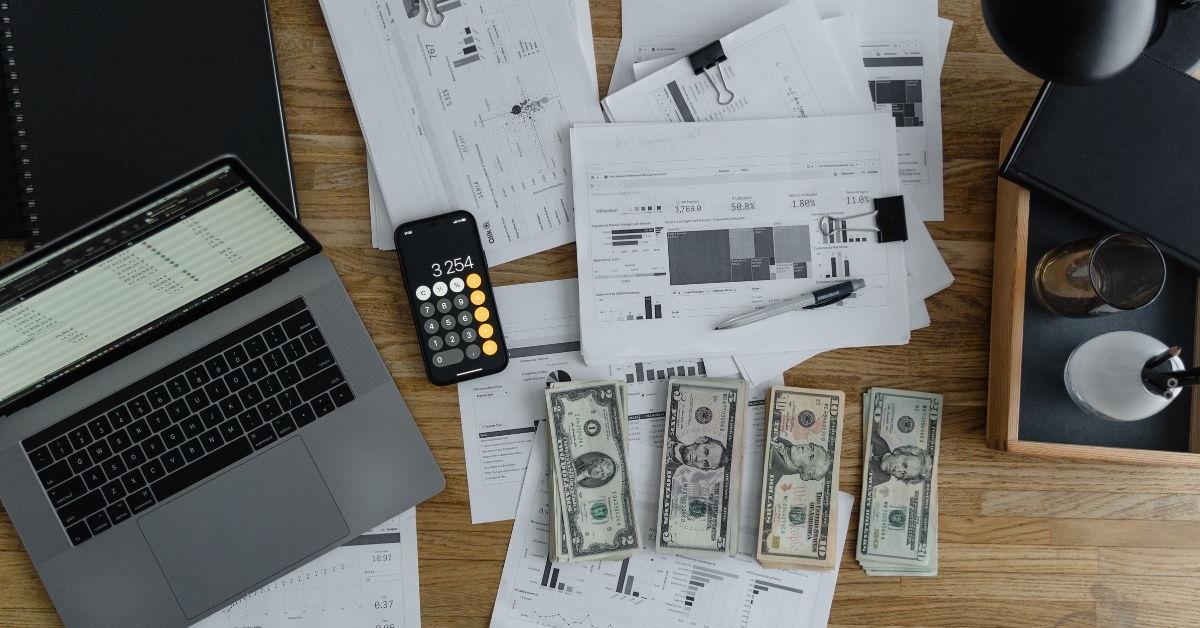 “Financial documents, cash, and laptop with calculator app open on desk for business accounting.”