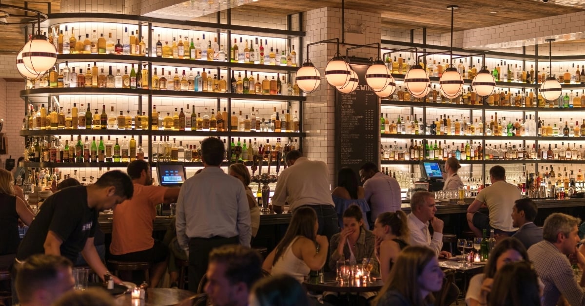 Busy bar interior with full shelves of liquor bottles and customers enjoying drinks
