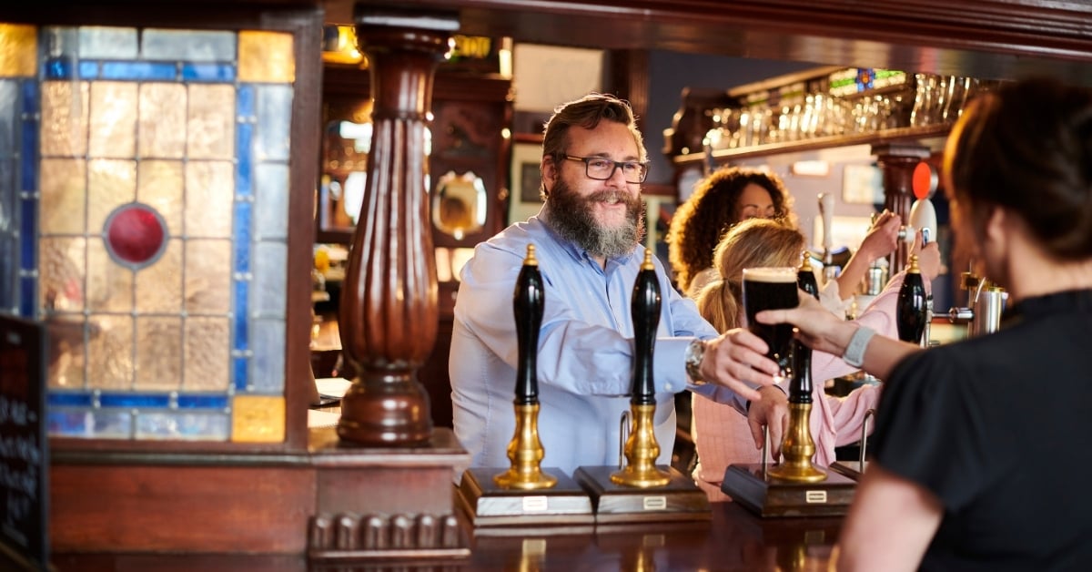 Happy pub owner serving pint of draft beer to customer